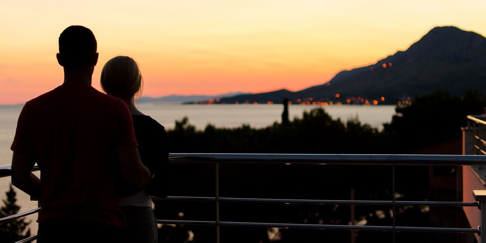A couple standing on a balcony, admiring the breathtaking sunset over the mountains and sea.