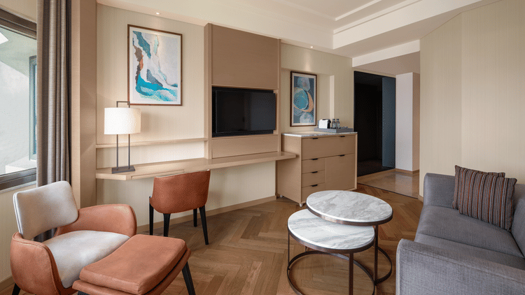 Inviting living area of a suite room at The Residency Chennai, featuring a large cozy sofa, a comfortable chair, a round table, and a wall-mounted TV.