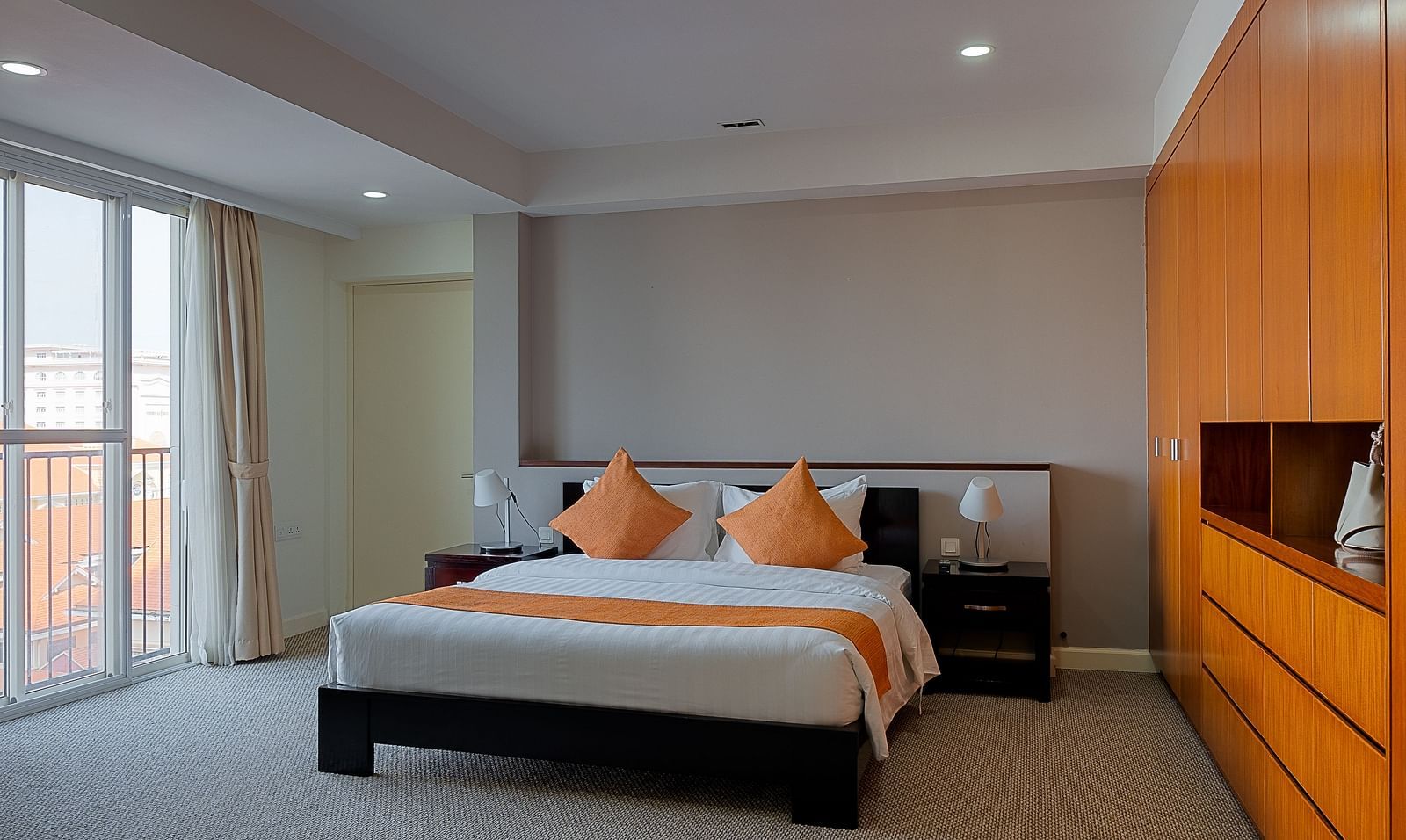 A bedroom with a bed, bedside tables, and an orange accent wall | Penthouse | Central Mansions, Phnom Penh
