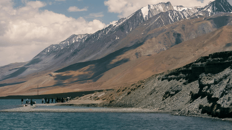 A lake flowing through the rugged mountains of Ladakh under a partly cloudy sky.