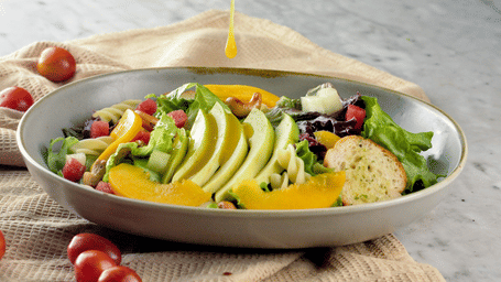 A plate of salad with sauce being poured over it.