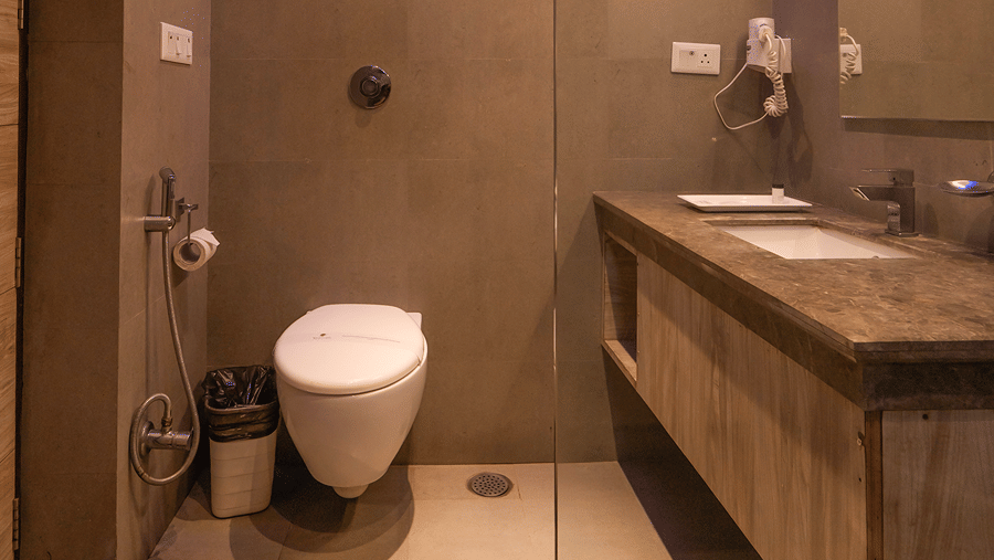 A sleek modern bathroom with grey tiled walls, blue ambient accent lighting, double vanity sink, and wall-mounted toilet - Wood Castle Spa & Resort, Jim Corbett