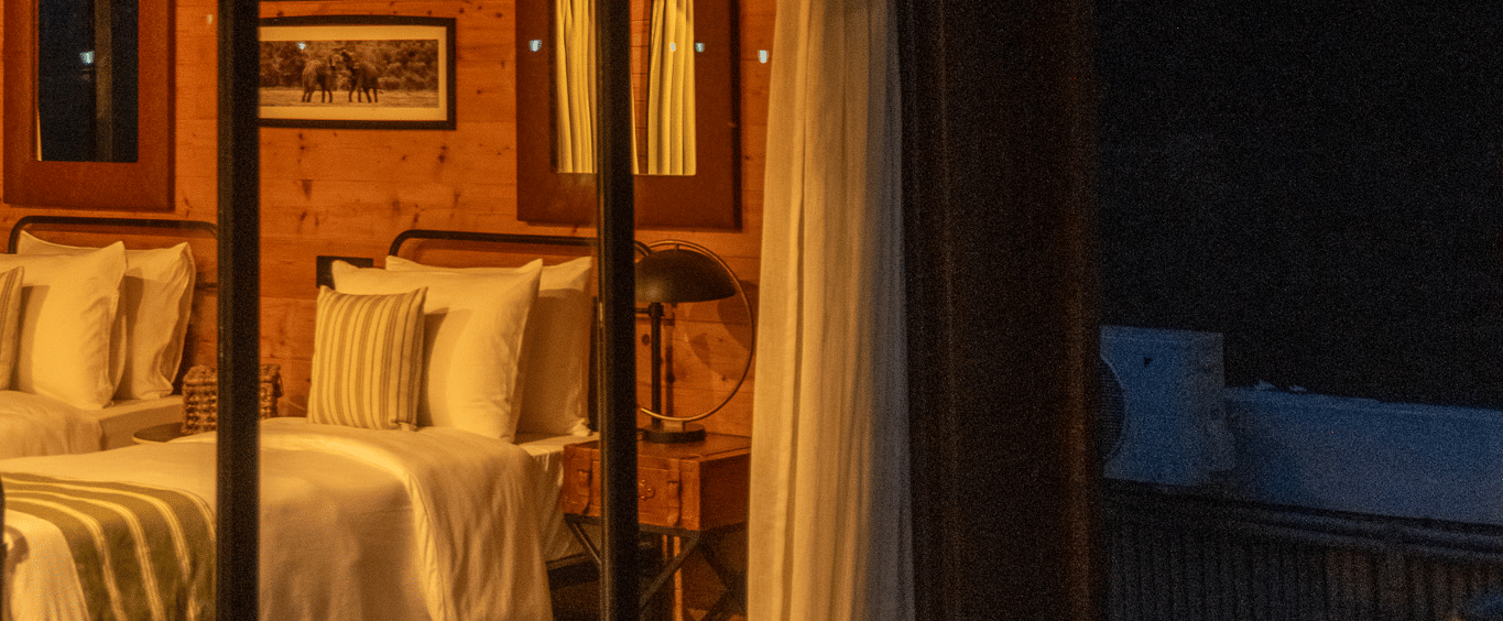 Cosy wooden cottage bedroom warmly lit with twin beds and rustic decor at Rhino and River BluSalzz Collection, Pobitora.