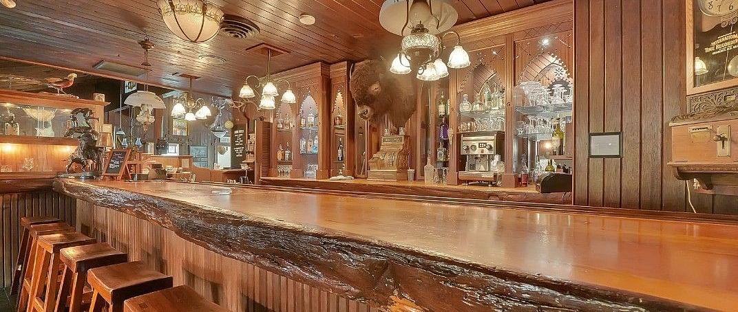 A warmly lit wooden bar at Shaver Lake Village Hotel with classic decor, vintage hanging lamps, and barstools lined along the counter.