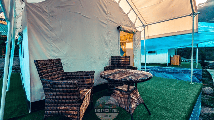 An outdoor seating area of a Luxury Tent at Dawat e Drung by FrozenFall Resort, Drung, Tangmarg, featuring artificial grass, an armchair, and a small table.