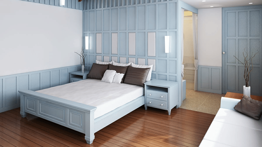 Hill Villa bedroom at Symphony Oceanus Bay Beach Resort & Spa with a pale blue panelled bed and wall, white linens, 4 pillows, and an ensuite bathroom beyond.