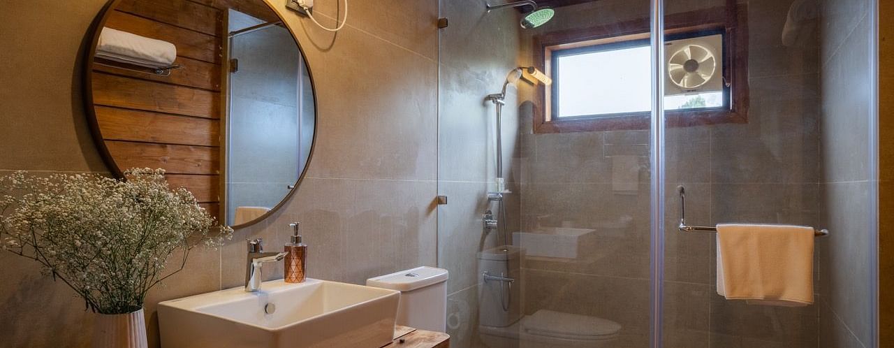 An image of a washroom with sink, faucet, mirror on the wall , shower screen, and a towel hanging inside the shower - Avalon Cottages, Kanatal