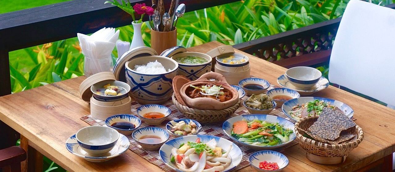 A wooden table set with a variety of traditional dishes in a garden setting - Alibu Resort Nha Trang