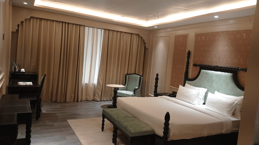 Bedroom with double bed, chairs, desk and curtains along the wall at Beelwa Palace, Jaipur