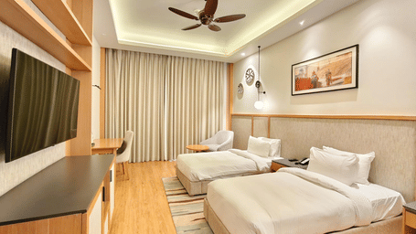 A modern hotel room featuring two neatly made twin beds, warm lighting, a ceiling fan, and a framed picture on the wall.