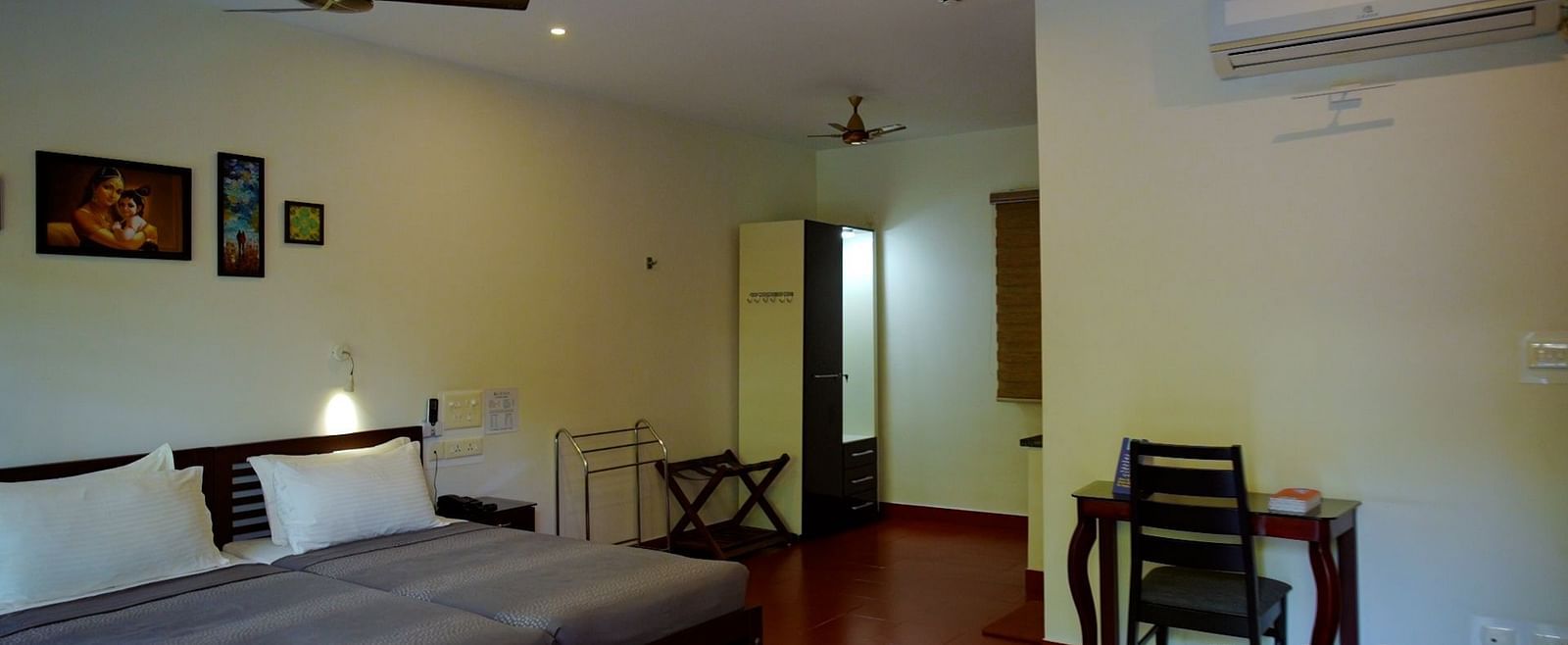 A simply furnished hotel room with a bed, desk, and ceiling fan.