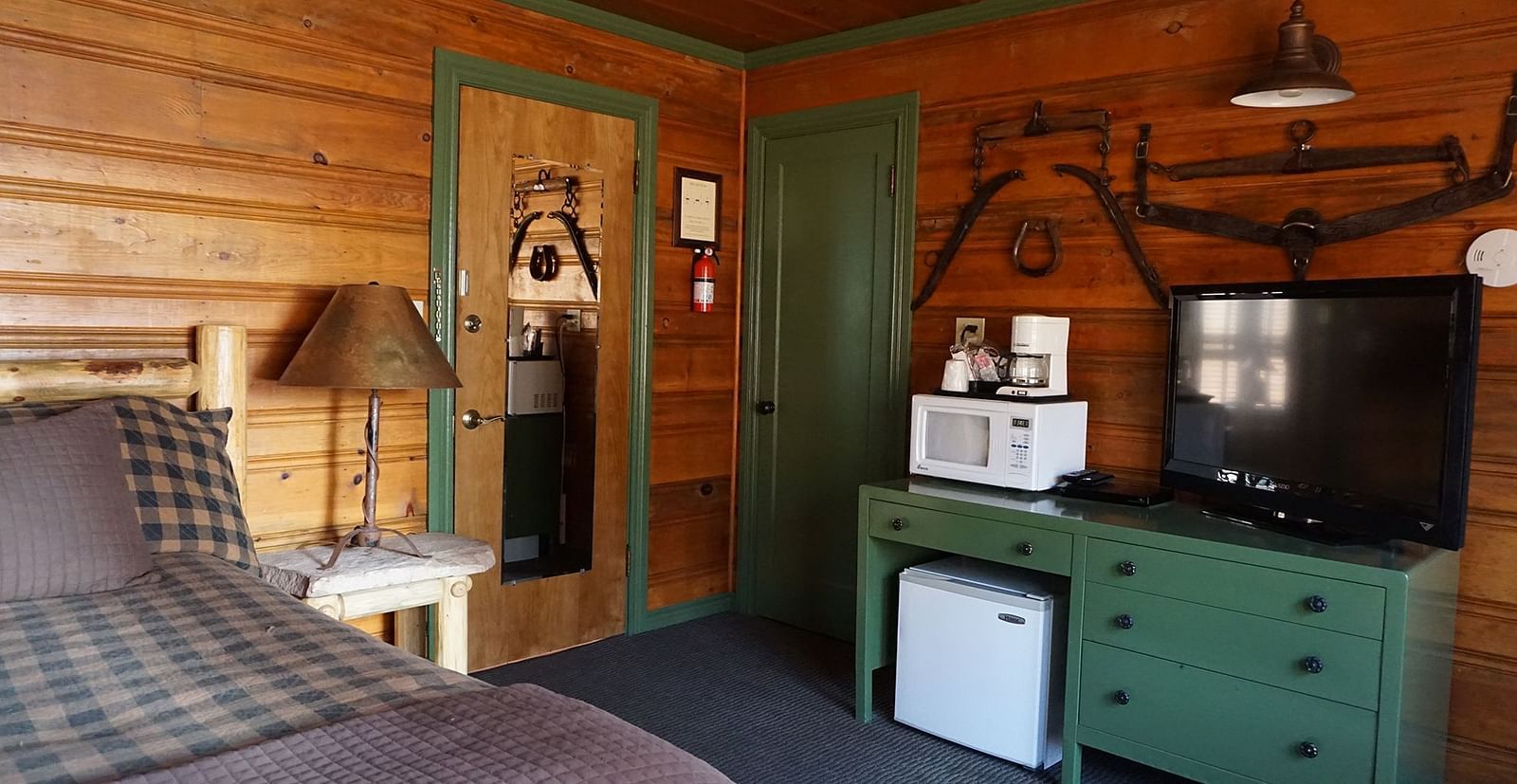 A room at Shaver Lake Village Hotel with a double bed, a lamp on a night stand, a green cabinet and wooden paneling throughout.