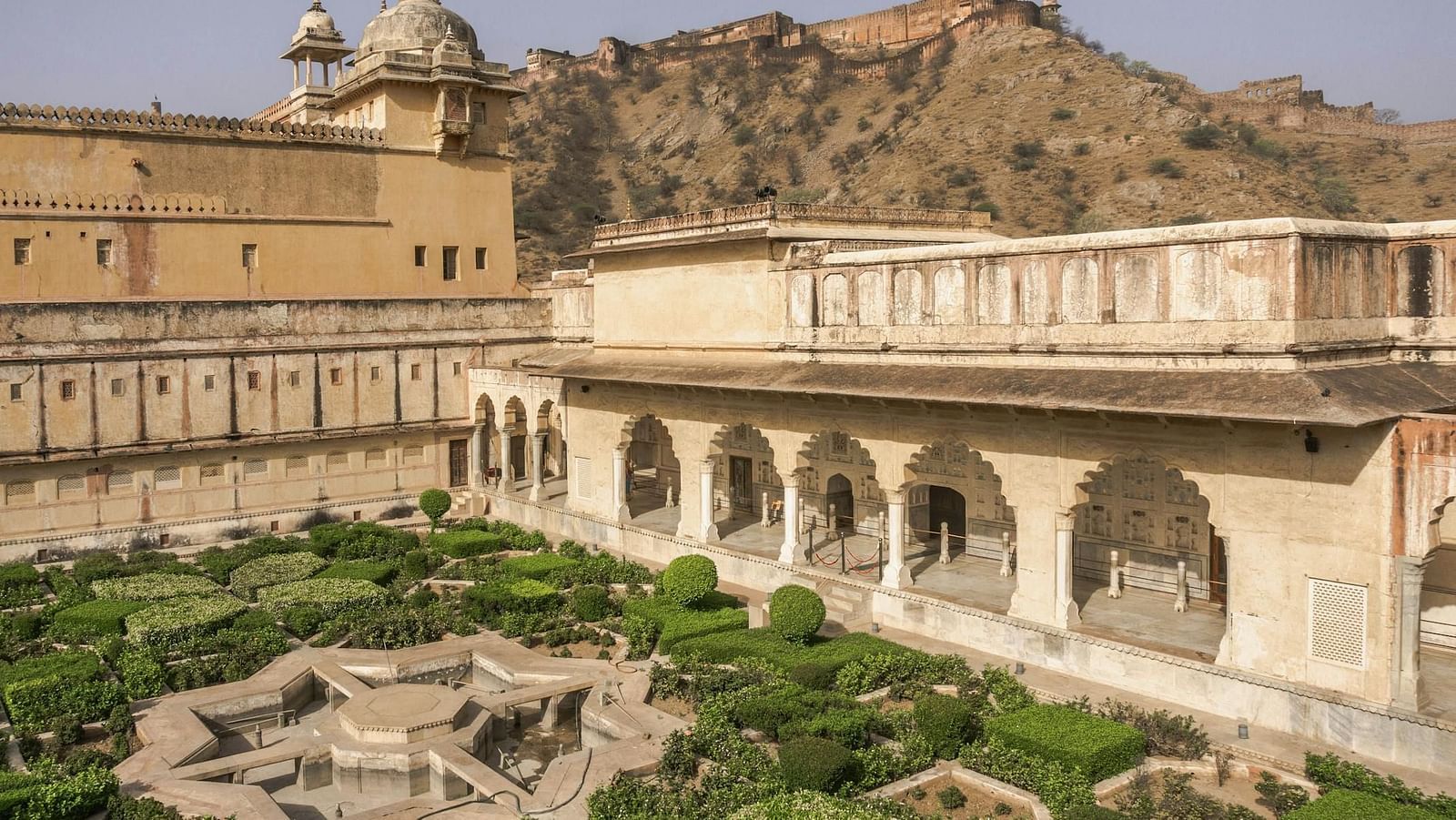 A scenic view of Amber Fort in Jaipur, Rajasthan, showcases its intricate architecture, a formal garden with water features, and the surrounding hills.