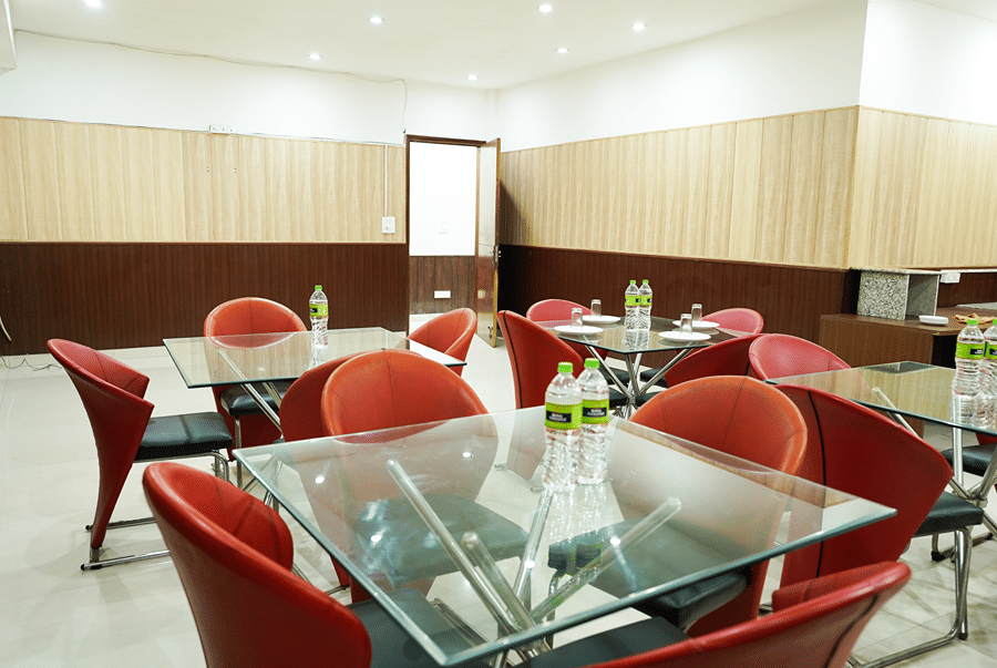 Dining space with red chairs and glass-topped tables at Lime Tree Hotel, IFFCO Chowk, Gurgaon