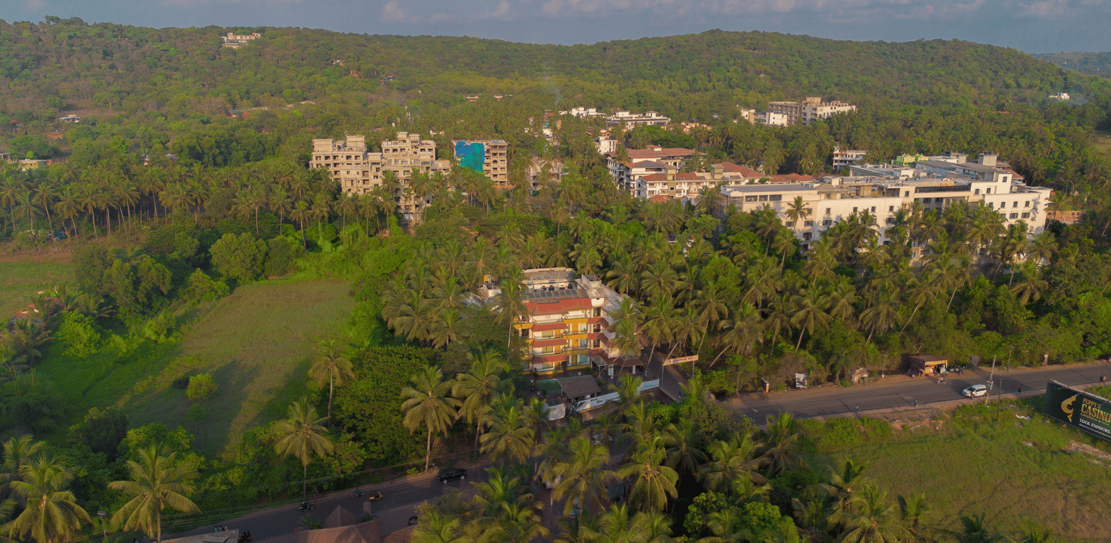 An aerial view showcasing a large hotel complex nestled among green fields and palm trees under a bright sky - Perfectstayz Premium Goa Continental