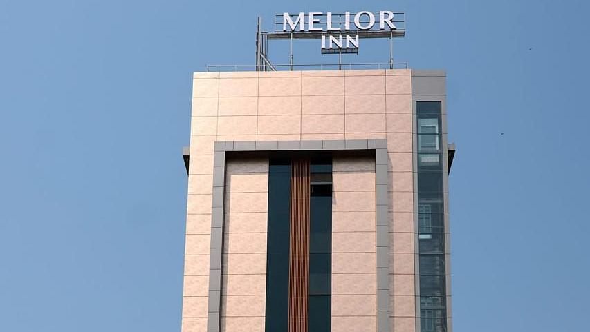 A tall, modern building against a clear blue sky, surrounded by some greenery - Melior Inn