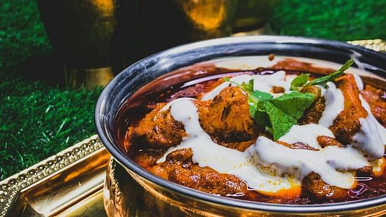 Bowl of rich, creamy chicken curry garnished with herbs.