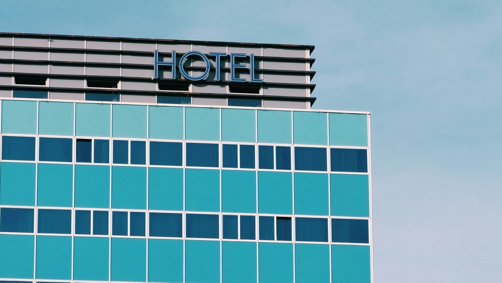 Close-up of the top of a modern high-rise office building with blue glass windows, featuring signage with the text in white letters against a turquoise sky.