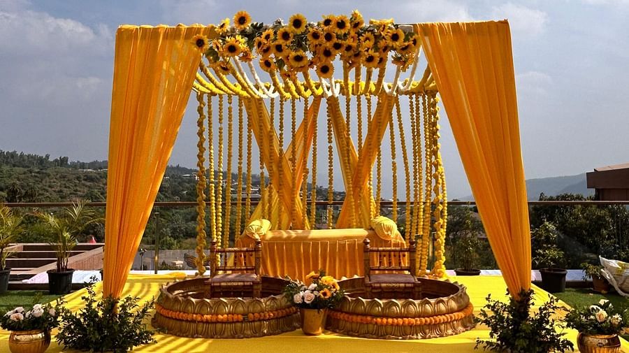 A place decorated with yellow fabrics and flowers with two  round seating areas where bride and groom sit during wedding rituals to apply turmeric on their skin - The Grand Legacy Resort & Spa 