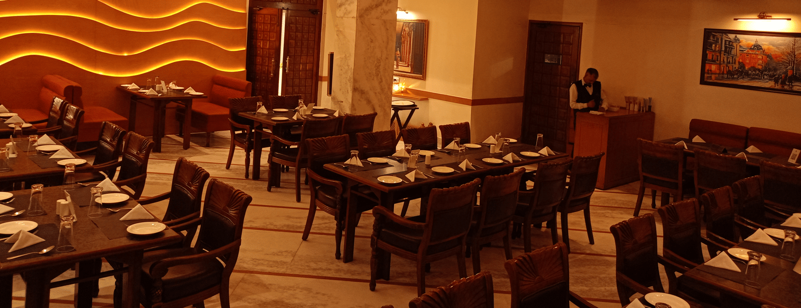 Dining area at Hotel Gold, Panipat featuring set tables, chairs, and a wavy patterned wall design.