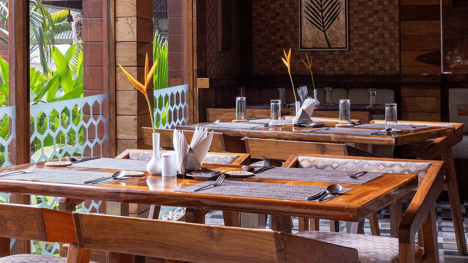 A spacious dining area at Ocean Prime with wooden tables and chairs, set in a modern wooden room. The decor is minimalist, with large windows offering a glimpse of the outside greenery - Coral Reef Resort & Spa, Havelock