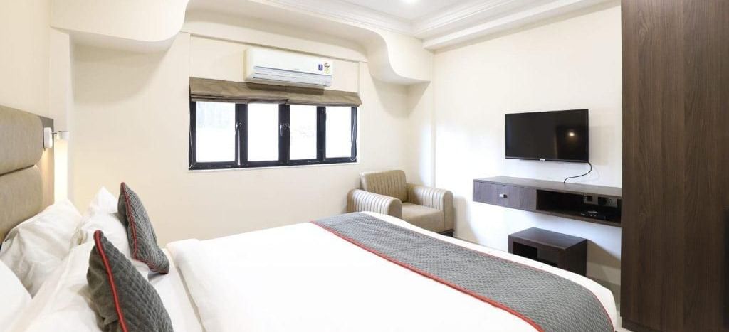 A wide-angle shot of the Premium Room at Pravasa Stay, Ahmedabad (Alba Premier), featuring a double bed along with a wall-mounted television.