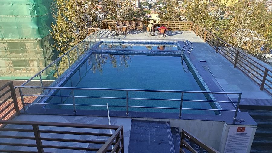 The swimming pool with clear water and a pool patio covered by safety railing and seating chairs at Two spa tables placed in a room with carpeted flooring, curtained windows, a chair and a table at Mandala Norling Lords Prime in Kathmandu.