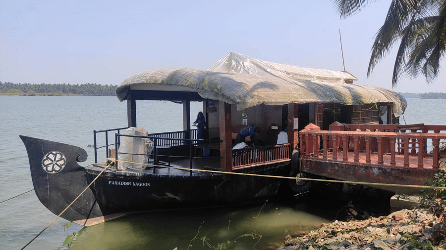 Houseboat with canopy roof anchored by the water at Paradise Lagoon Resort, Udupi.