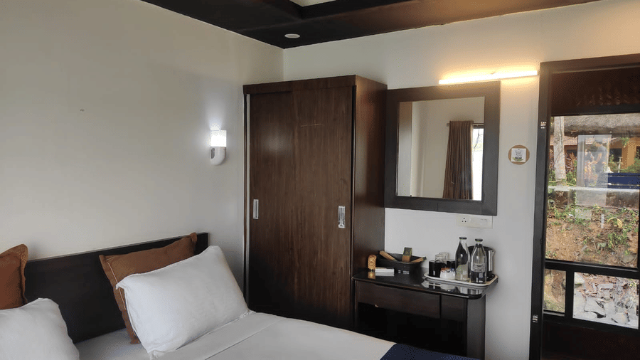 Bedroom with a queen bed, mirror, and wall-mounted light at Paradise Lagoon Resort, Udupi.
