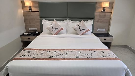 A well-lit deluxe room in Clarks Inn Express, Firozabad, featuring a king size bed, neatly made with patterned runner.