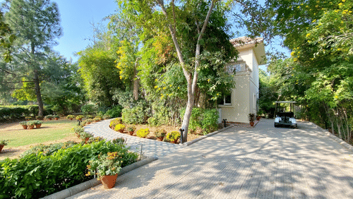 A huge house with green trees and lawn inside the compound, pictured with a golf cart parked on the front of the house - Karma Lakelands.
