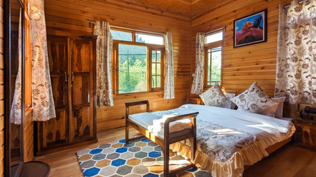 1BHK Villa bedroom at Dawat e Drung by FrozenFall Resort, Drung, Tangmarg, showing 1 double bed, a wooden wardrobe, window curtains, and a patterned rug.