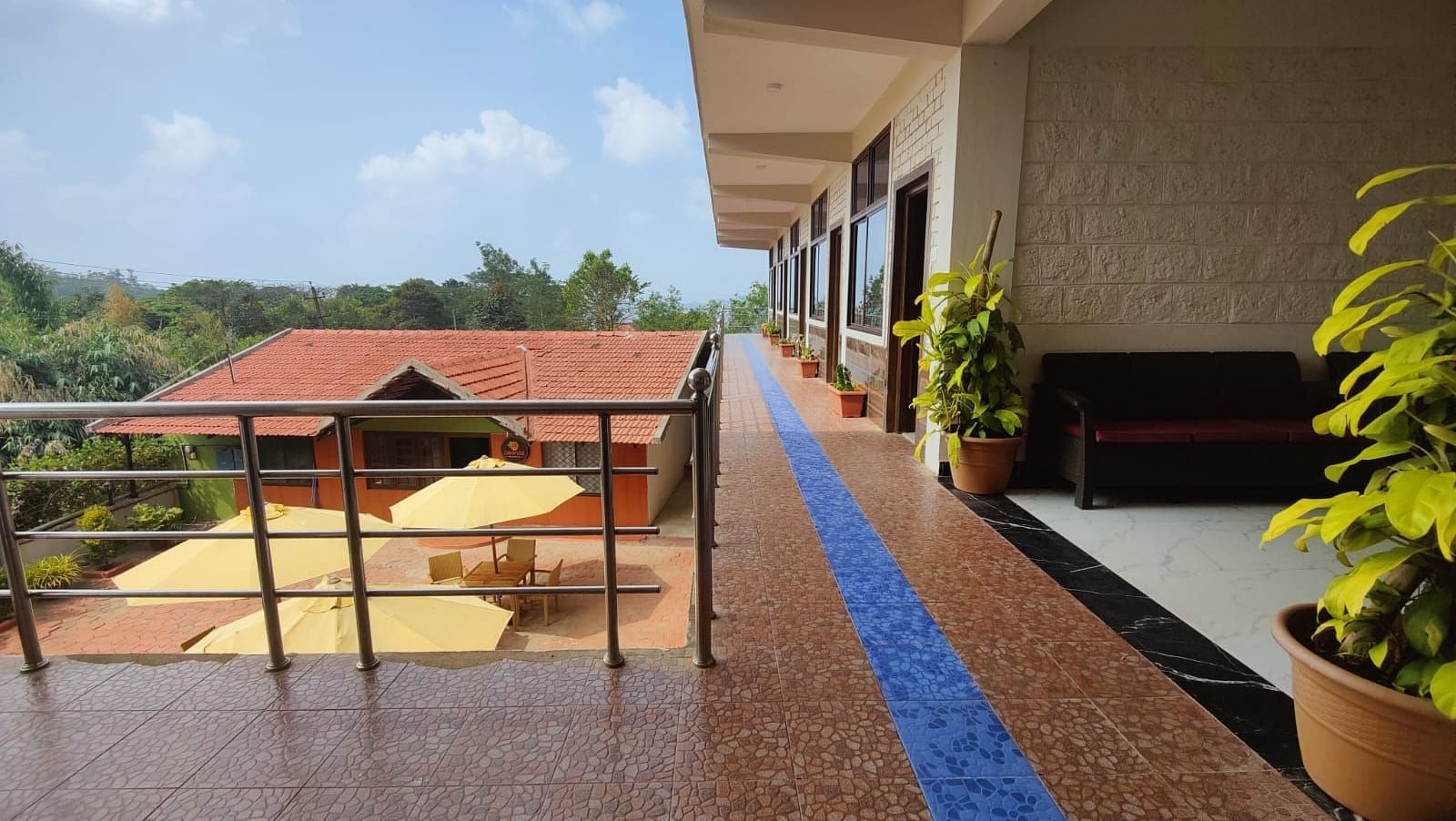 Tiled balcony with sofa and potted plants that overlooks a house, patio and greenery | Standard Room |  Woodstock Resorts, Coorg