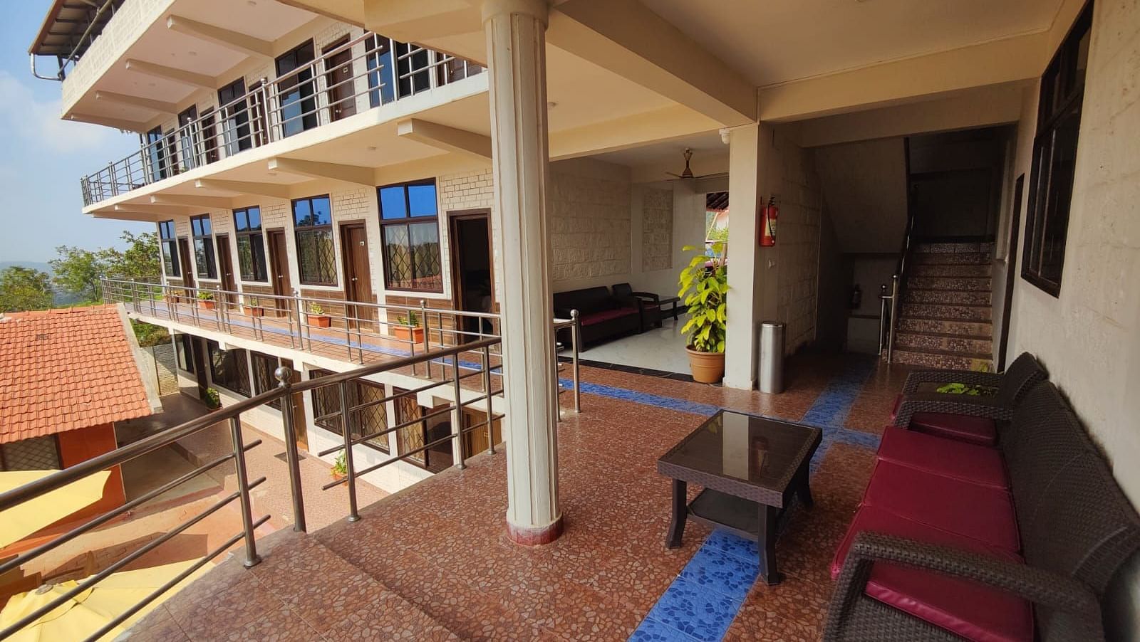Tiled balcony with sofa and potted plants that overlooks a house, patio and greenery | Standard Room| Woodstock Resorts, Coorg