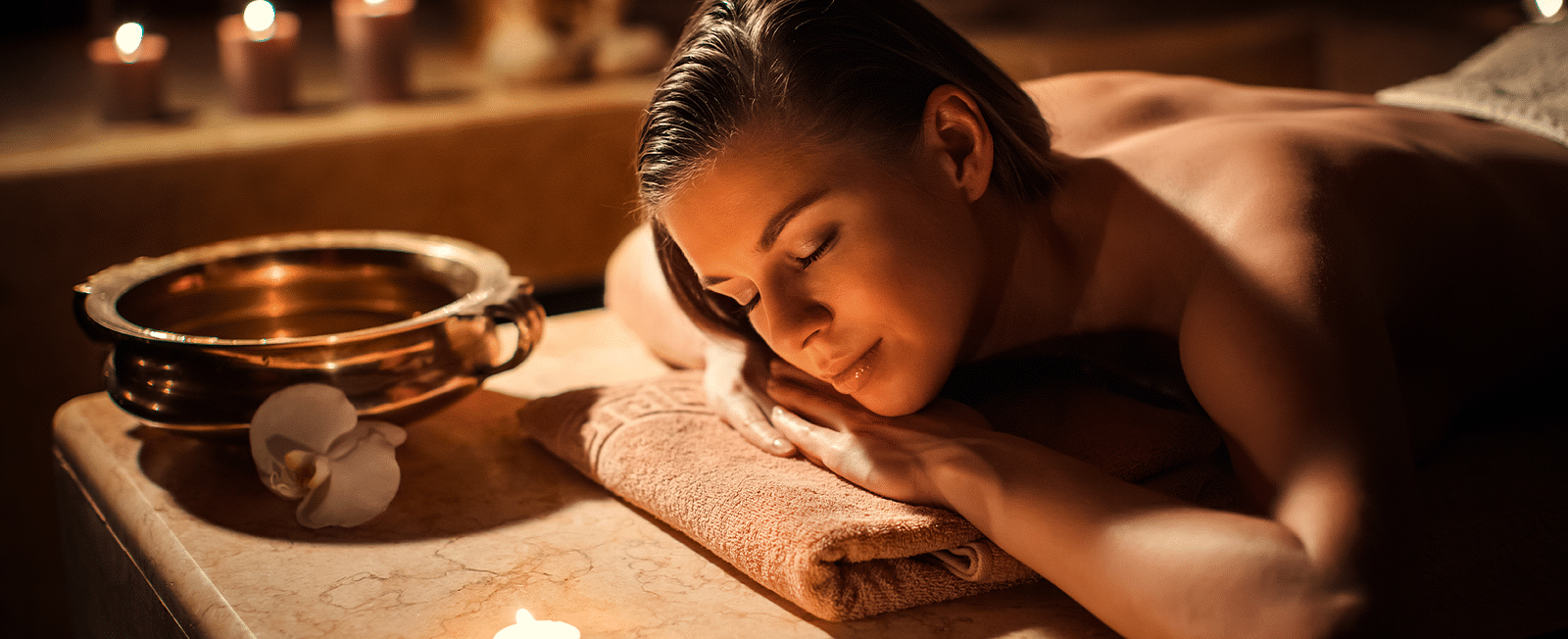 Woman relaxing during a spa treatment surrounded by candles, enjoying a moment of calm