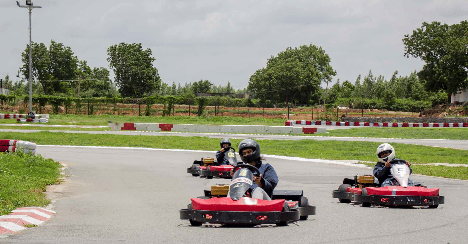3 people enjoy racing go-karts around a curved outdoor track - District Gravity Adventure Park, Hyderabad