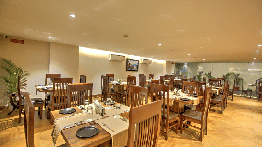 A dining area with warm ambient lighting, featuring light wood floors and organised clusters of wooden dining sets - Hotel 91 HUDA City Centre, Gurugram