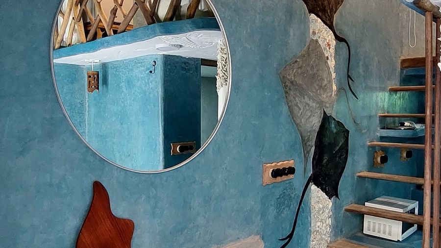 circular mirror near the stairs, the wall and floor both are painted in blue and some flower structures have been added to the wall, near a small seating area attached to wall.