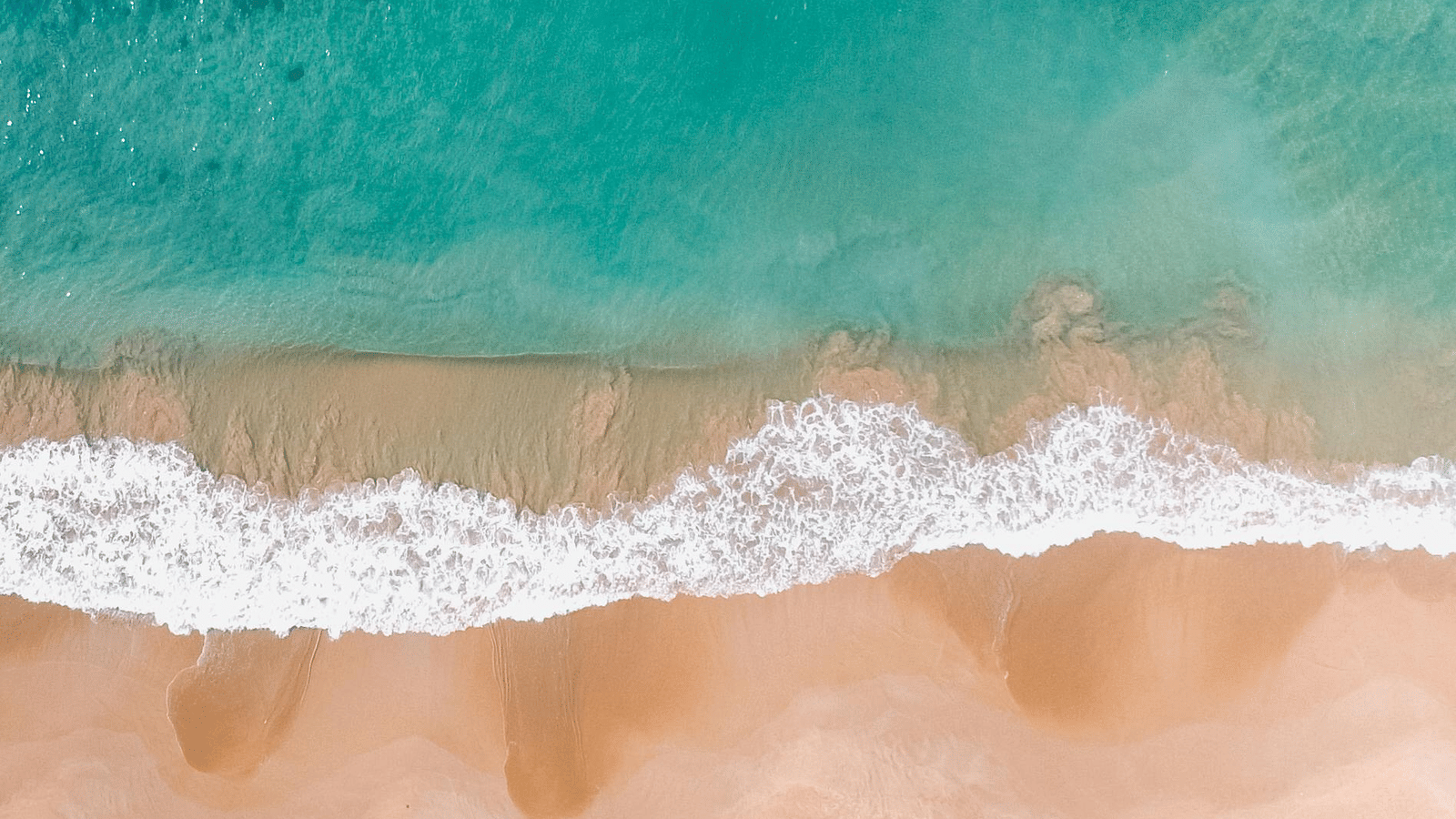 Aerial view of a golden sandy beach meeting turquoise waves along a coastline.