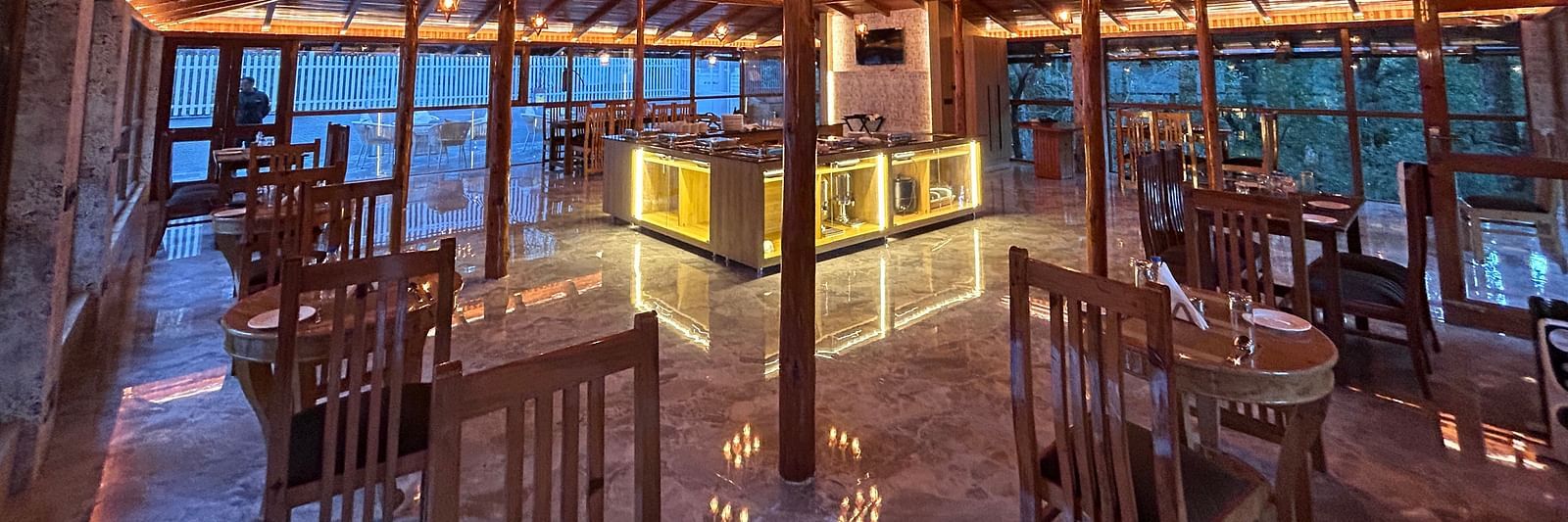 An image of the restaurant at DLS The Emerald, Nainital with wooden interiors along with chairs and tables and the area is lit with bright lighting