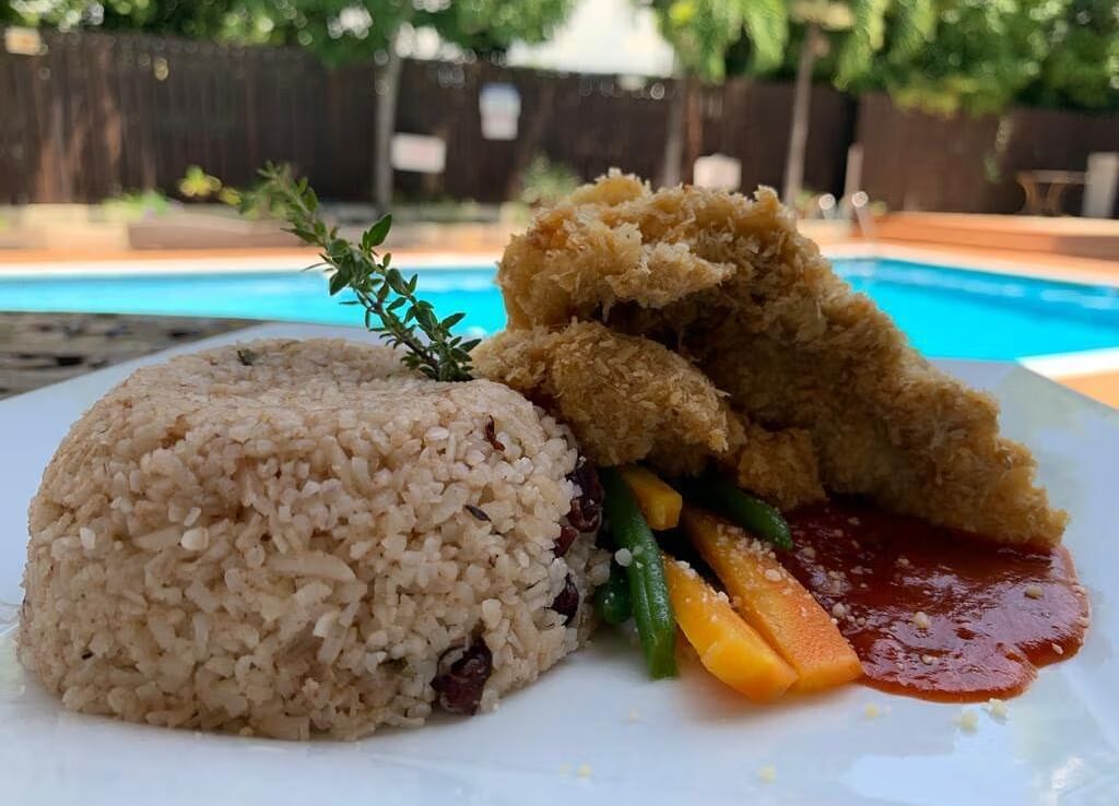 A plate with rice and a piece of fried fish or chicken, served by a swimming pool | Altamont Court, Jamaica