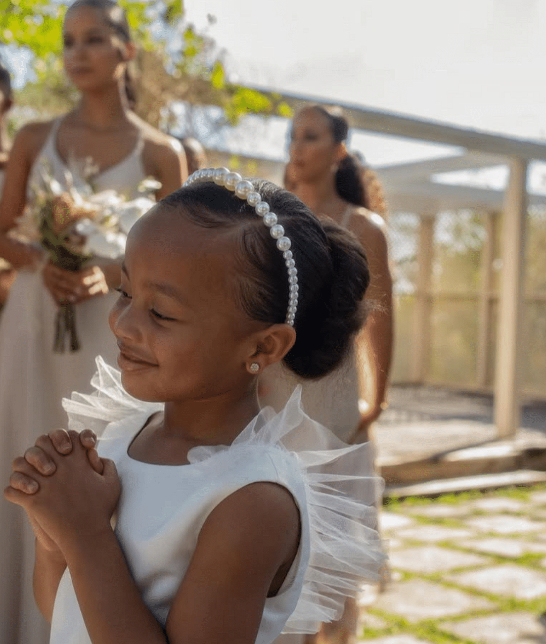 A young girl in white dress standing in front of bridesmaids in beige dresses outdoors | A Stone's Throw Away