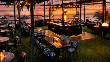 An outdoor rooftop or waterfront restaurant and bar at sunset.