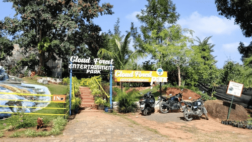Entrance of Cloud Forest Park with signboard and motorcycles parked nearby.