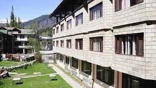 The exterior of  DLS Kapoor Resorts Manali showcases a building with balconies overlooking a lush green lawn.