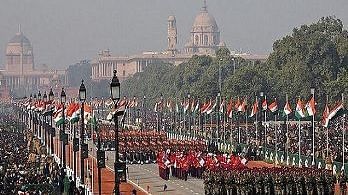 An aerial view captures the India Republic Day Parade on Kartavya Path (formerly Rajpath) in New Delhi, featuring marching contingents and spectators, with a large government building in the background. 