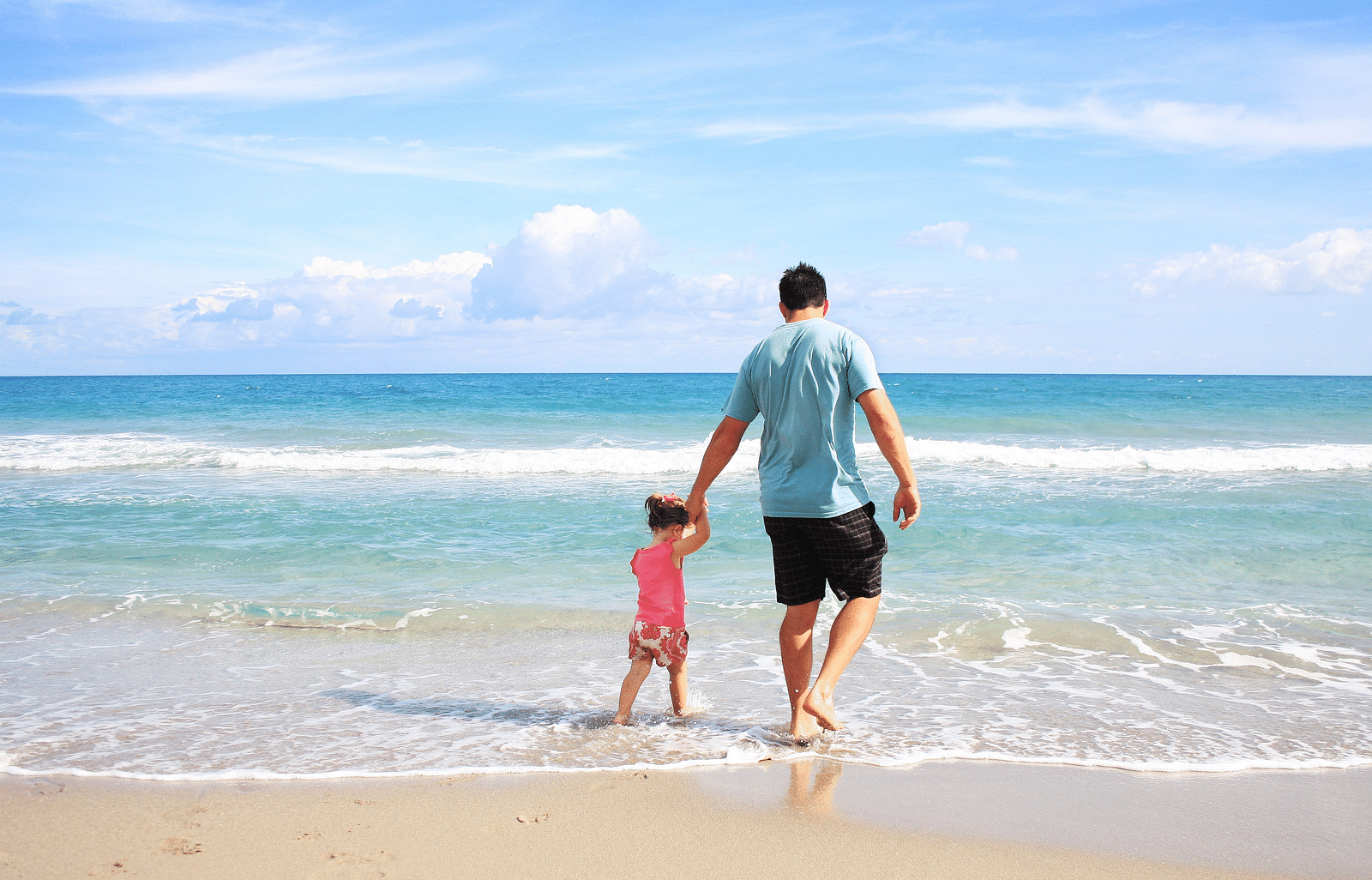 Father and daughter walking hand in hand along the beach shoreline.