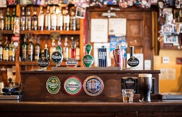 A pub interior with a wooden bar, beer taps, bottles on shelves, and various coasters and glasses.