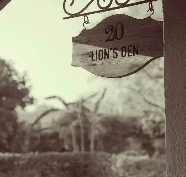 Sepia-toned image of a wooden sign reading  Lion's Den on the grounds of Karma Chalets.