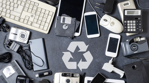An aerial view of many tech items kept on a table with the recycle symbol in the centre - Karma Lakelands.